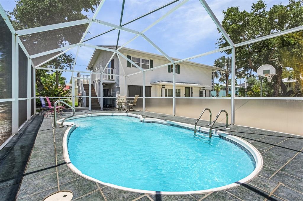 An outdoor swimming pool is enclosed by a screened lanai next to a two-story house — 140 BAY MAR DRIVE, FORT MYERS BEACH, FL