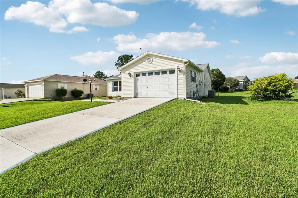 A single-story house with light siding, a white garage door, and a concrete driveway — 8544 SE 177TH BARTRAM LOOP, THE VILLAGES, FL