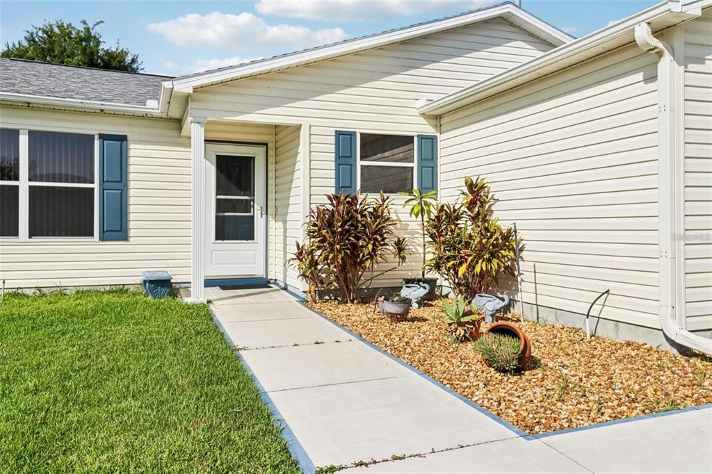 A concrete walkway leads to the front door of a beige vinyl-sided house — 8544 SE 177TH BARTRAM LOOP, THE VILLAGES, FL