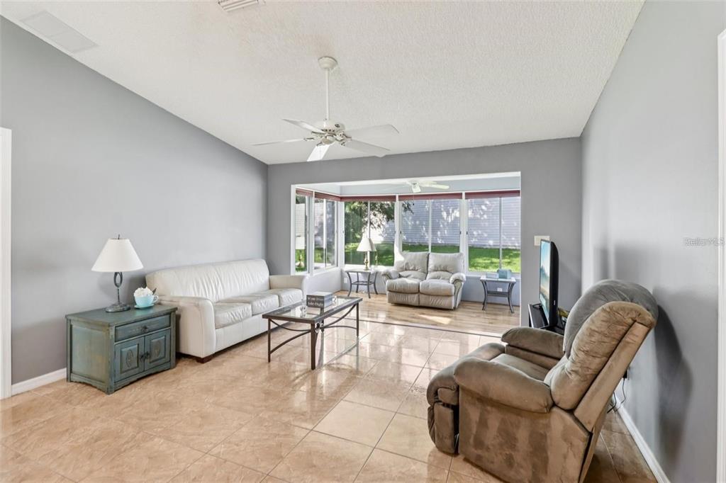 A living room with tile floors, a white sofa, a recliner, and a sunroom beyond — 8544 SE 177TH BARTRAM LOOP, THE VILLAGES, FL