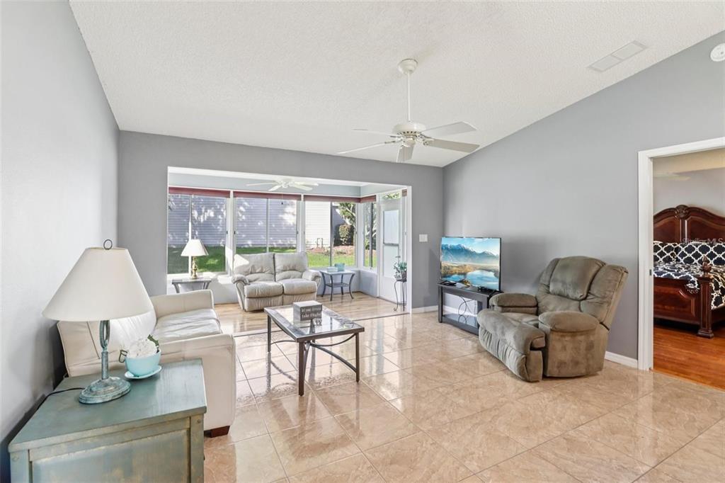 A living room with tile floors, a ceiling fan, and a view into a sunroom — 8544 SE 177TH BARTRAM LOOP, THE VILLAGES, FL