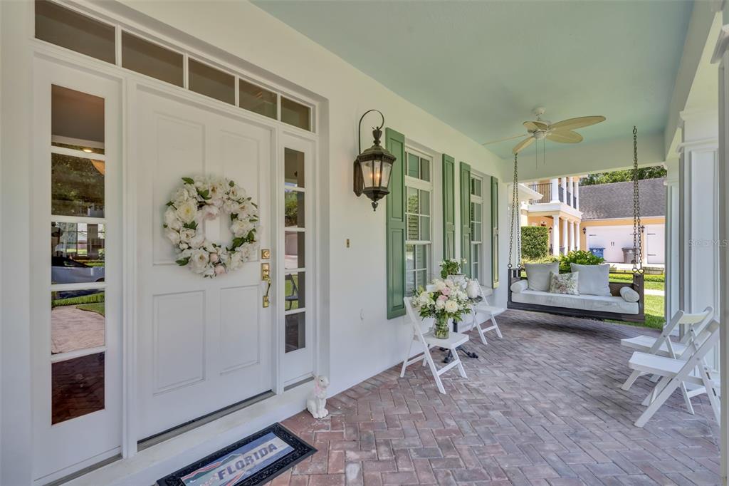 A covered brick porch features a white front door, a hanging swing, and green shutters — 2625 PARK PLACE DRIVE, WINTER PARK, FL