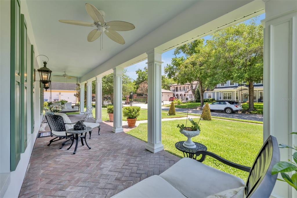 A covered brick porch features white columns, ceiling fans, and outdoor furniture overlooking a front yard — 2625 PARK PLACE DRIVE, WINTER PARK, FL