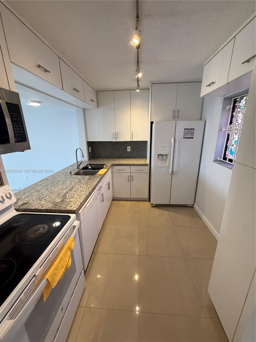 A kitchen features white cabinets, granite countertops, a tiled backsplash, and white appliances — 8625 NW 8th St # 420, Miami FL 33126, MIAMI, FL