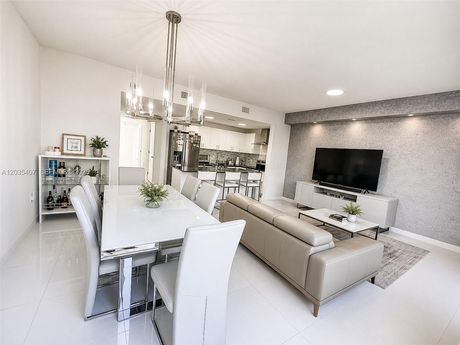 A modern open-concept living and dining area features white tile floors and a gray accent wall — 14467 SW 260th St, Homestead FL 33032, HOMESTEAD, FL