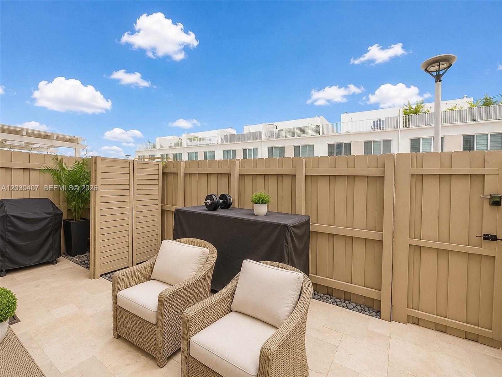 A patio features two wicker chairs, a covered table with dumbbells, and a wooden fence — 14467 SW 260th St, Homestead FL 33032, HOMESTEAD, FL
