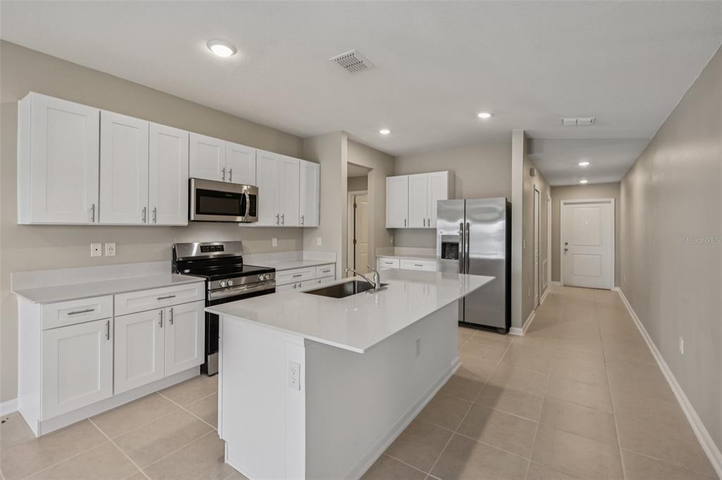 A kitchen features white cabinets, stainless steel appliances, a center island, and light tile flooring — 1172 BELLE ISLE LANE, DAYTONA BEACH, FL