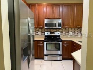 A kitchen with stainless steel appliances, wood cabinets, and a tiled backsplash — 20418 NEEDLETREE DRIVE, TAMPA, FL