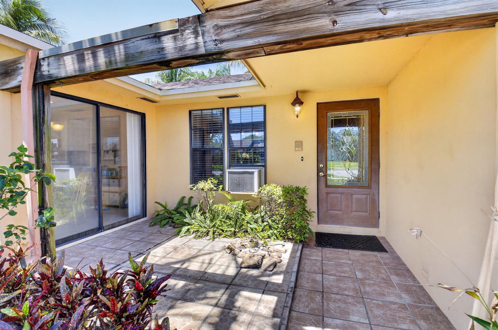 A tiled entryway features a wooden front door, a sliding glass door, and a window unit — 9389 Longmeadow Circle, Boynton Beach FL 33436, BOYNTON BEACH, FL