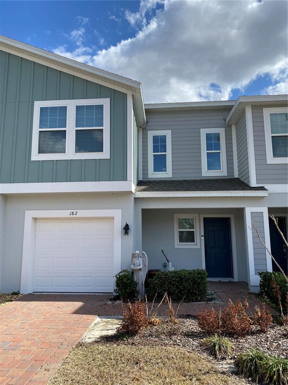 The exterior of a two-story townhouse features a garage, a blue door, and light-colored siding — 182 GLASS ONION DRIVE, HOWEY IN THE HILLS, FL
