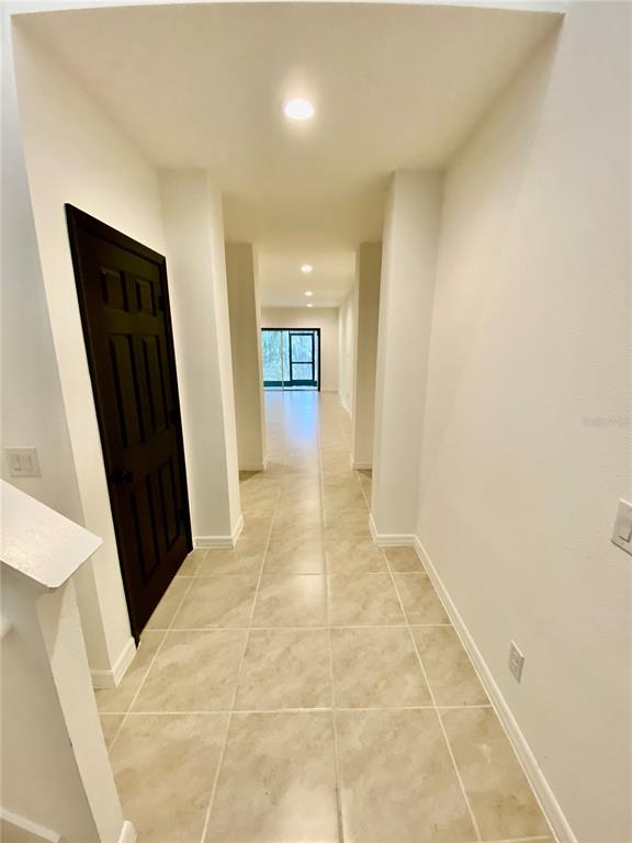 A hallway with light-colored tile flooring leads toward a glass door at the far end — 182 GLASS ONION DRIVE, HOWEY IN THE HILLS, FL
