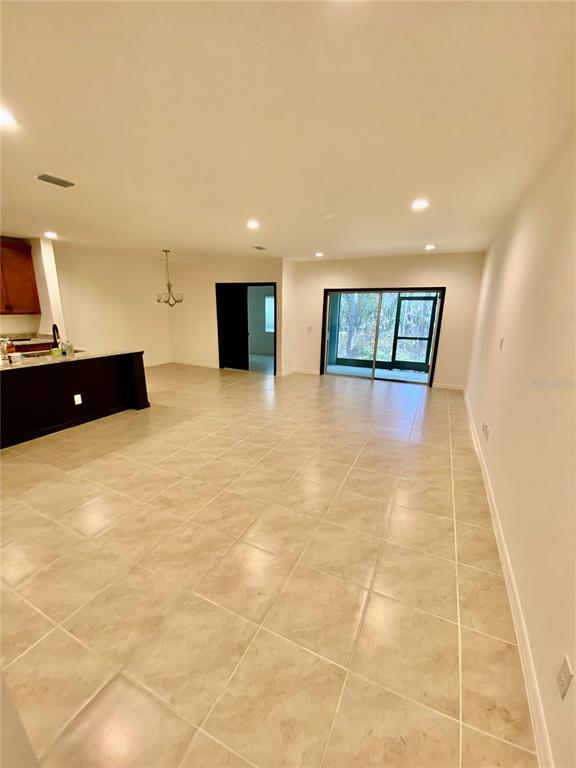 An open-concept living area features light-colored tile flooring, recessed lighting, and a sliding glass door — 182 GLASS ONION DRIVE, HOWEY IN THE HILLS, FL