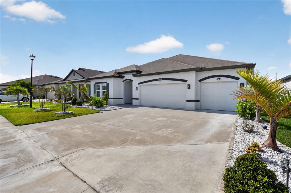 A single-story house with a three-car garage, white stucco exterior, and a concrete driveway — 2526 SAND GABLES TRAIL, BRADENTON, FL