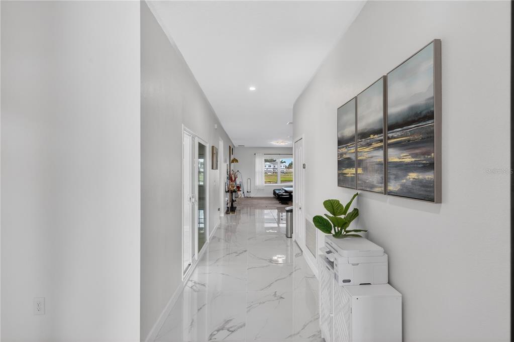 A long hallway with white marble-look tile flooring leads toward a bright living area — 2526 SAND GABLES TRAIL, BRADENTON, FL