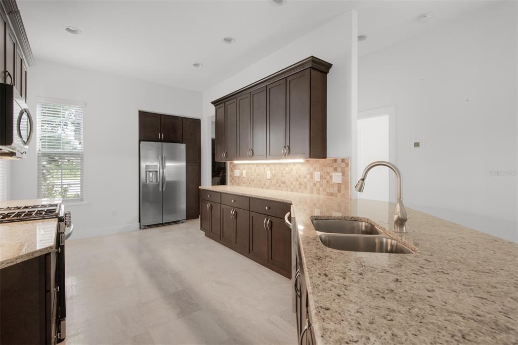 A kitchen features dark wood cabinets, granite countertops, stainless steel appliances, and a tiled backsplash — 9129 S DEER PARK DRIVE, HOMOSASSA, FL