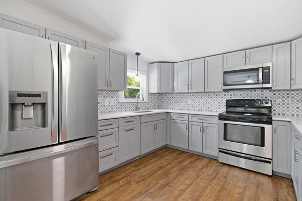 A kitchen with grey cabinets, stainless steel appliances, a patterned backsplash, and wood-look flooring — 24225 DUFFIELD ROAD, BROOKSVILLE, FL