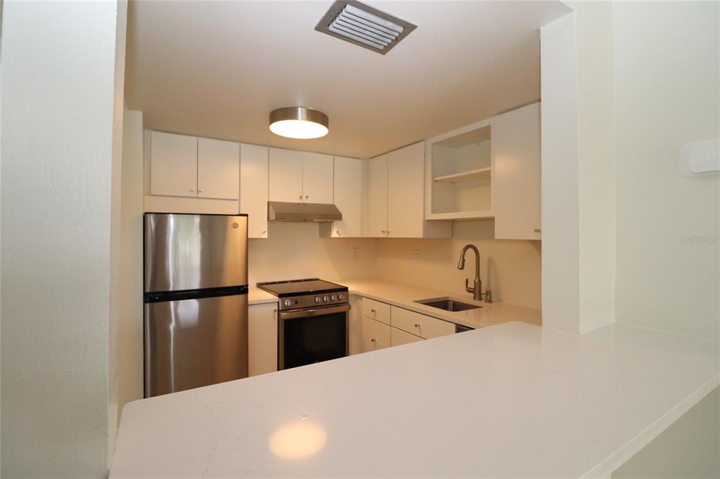 A kitchen features white cabinets, stainless steel appliances, and a white countertop breakfast bar — 618 ORANGE DRIVE UNIT 207, ALTAMONTE SPRINGS, FL