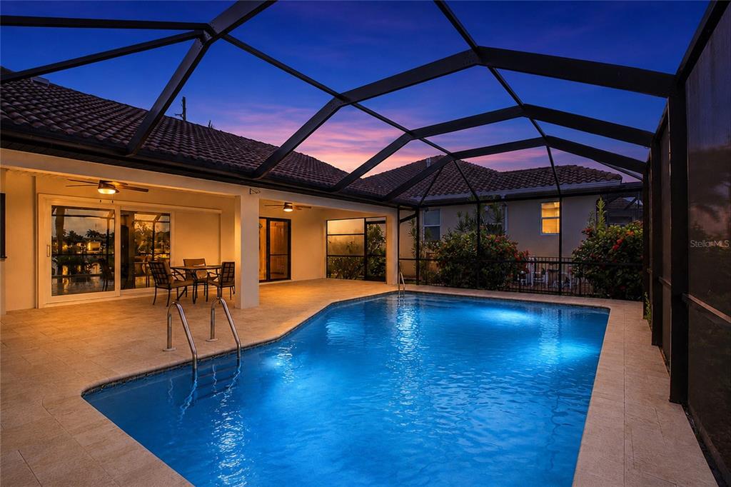 A screened-in patio features a swimming pool, outdoor dining area, and tile flooring at dusk — 454 MONACO DRIVE, PUNTA GORDA, FL