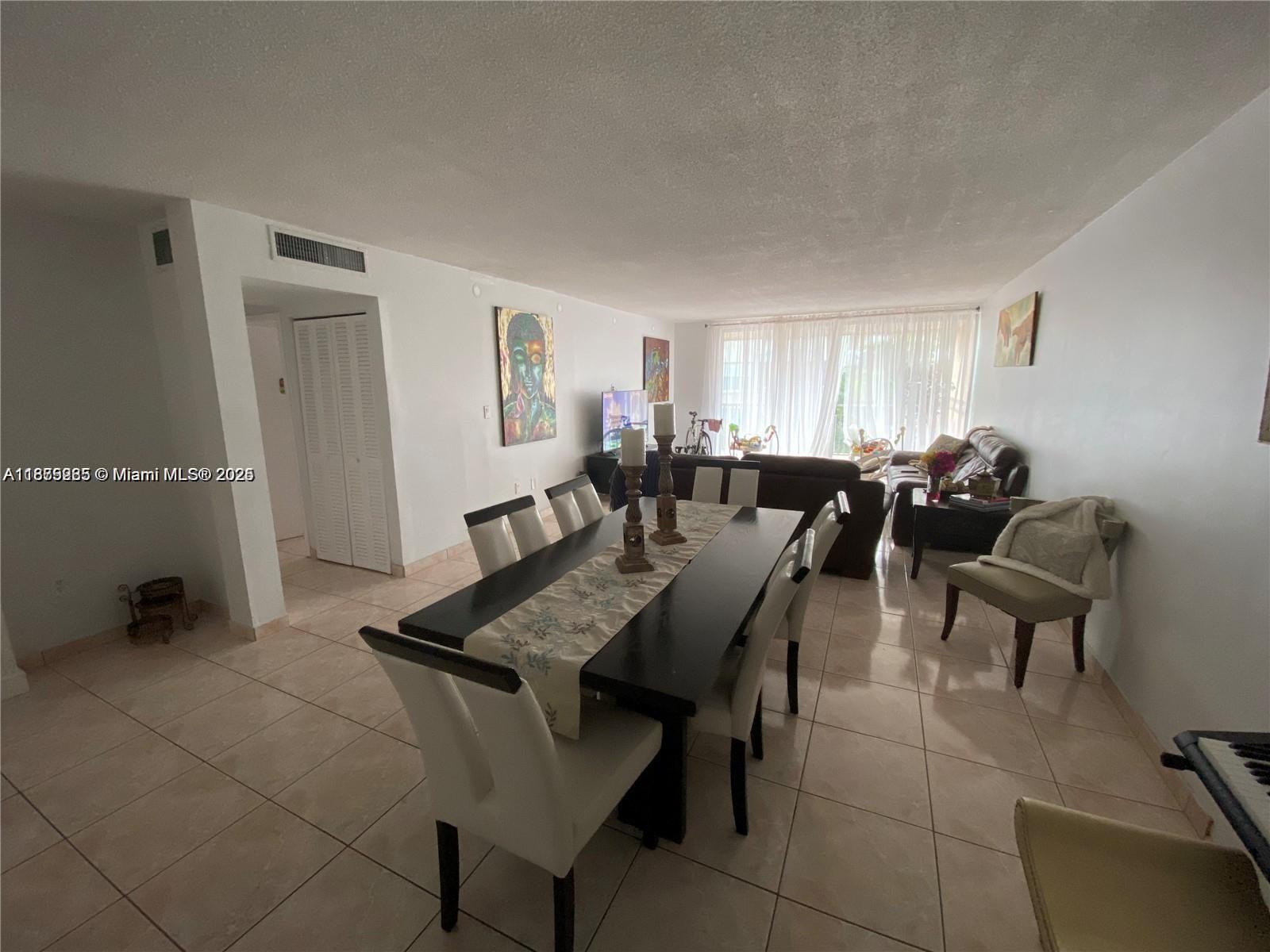 A dining area with a dark table and chairs sits in front of a living room — 1670 NE 191st St # 3, Miami FL 33179, MIAMI, FL