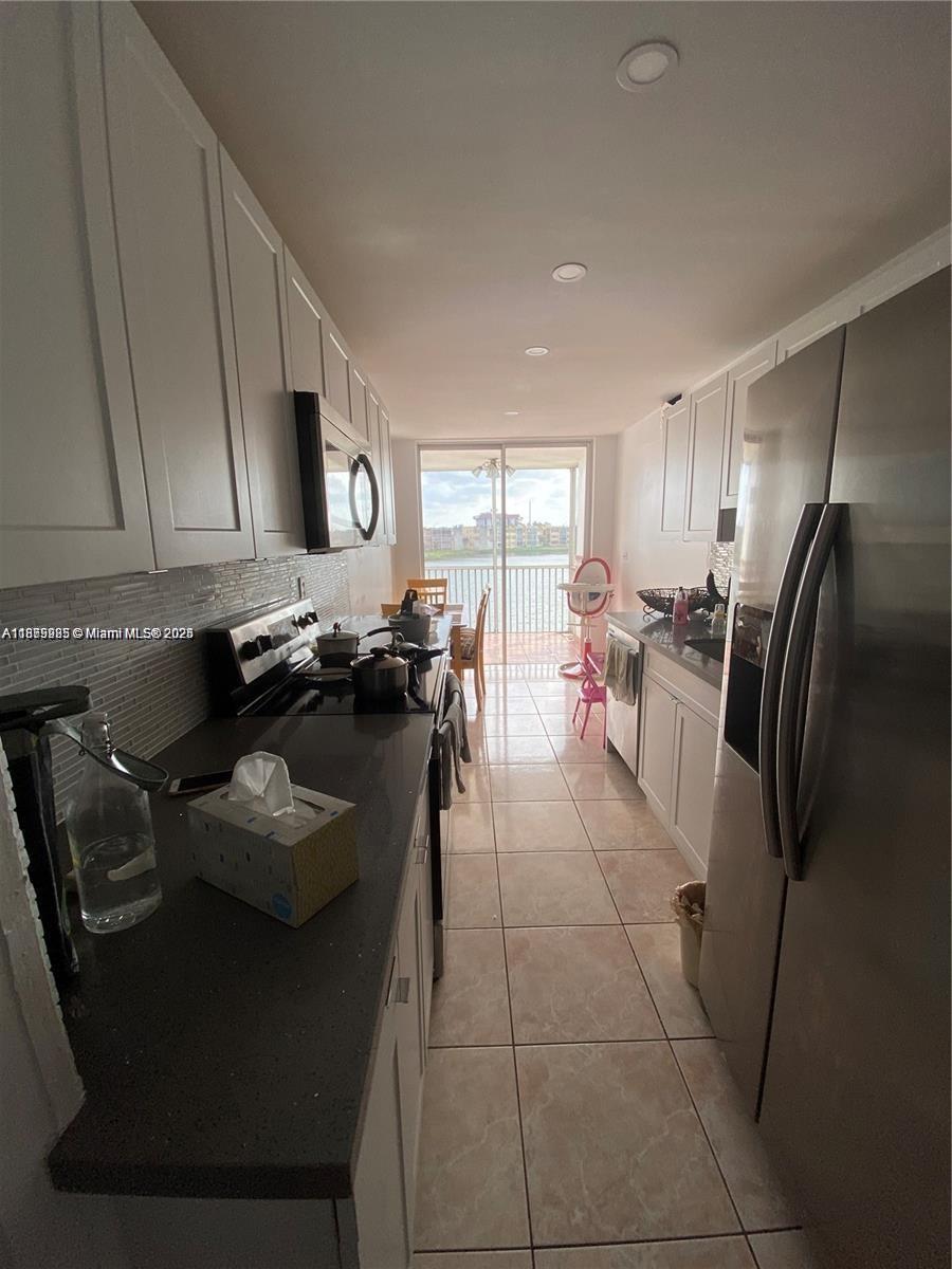 A narrow galley kitchen features white cabinets, dark countertops, stainless steel appliances, and a balcony — 1670 NE 191st St # 3, Miami FL 33179, MIAMI, FL