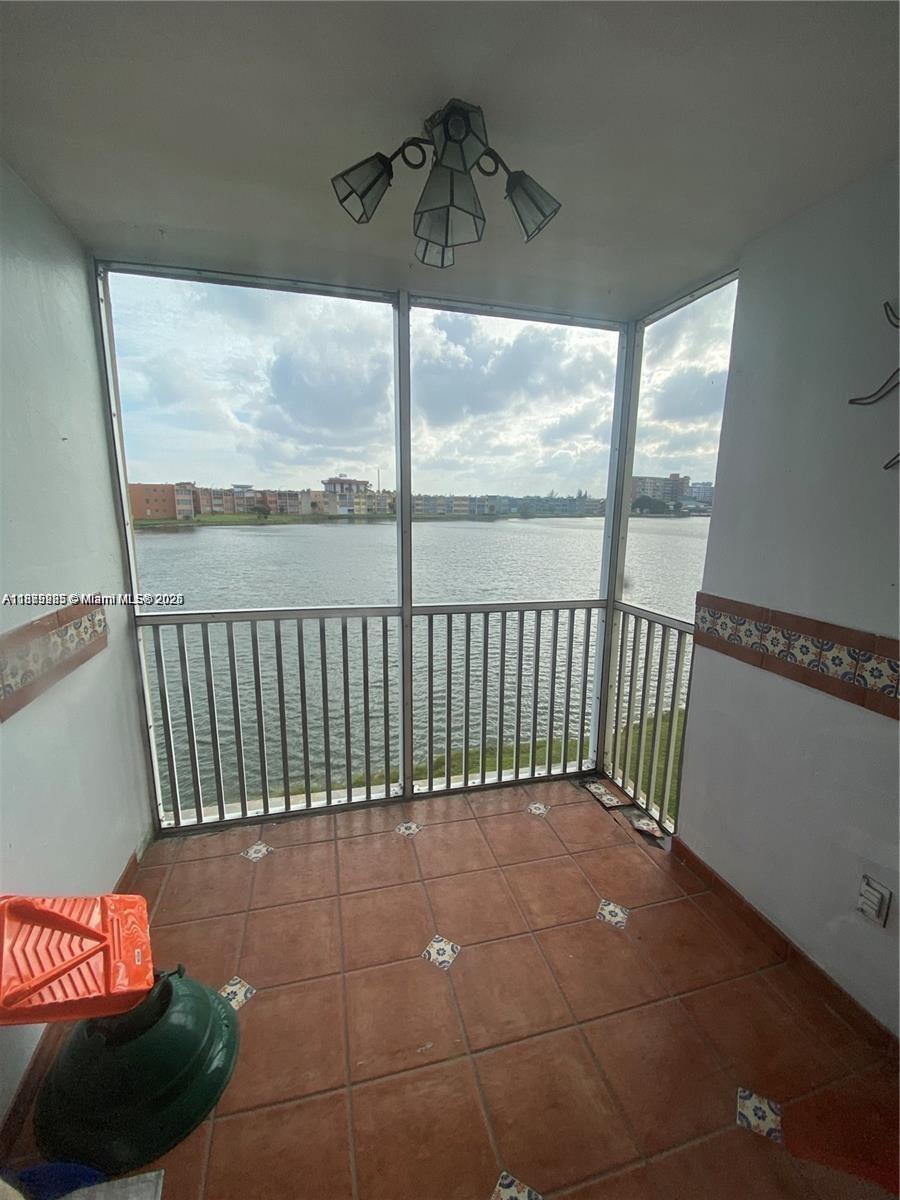 A screened-in balcony features terracotta tile flooring, decorative wall tiles, and a view of a lake — 1670 NE 191st St # 3, Miami FL 33179, MIAMI, FL