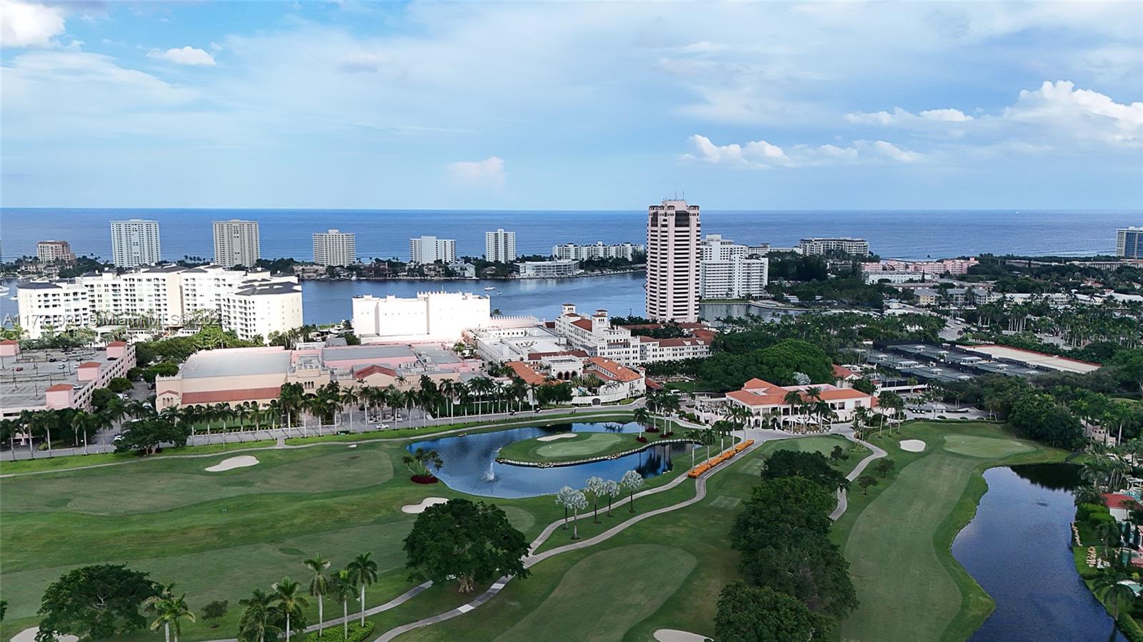 An aerial view shows a golf course with ponds, surrounding buildings, and the ocean beyond — 105 E Camino Real # 912, Boca Raton FL 33432, BOCA RATON, FL