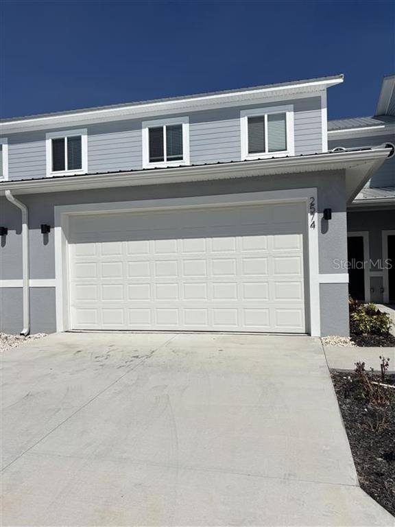 A two-story townhouse exterior features a white garage door, gray siding, and a concrete driveway — 2574 PINE PLACE, WINTER HAVEN, FL