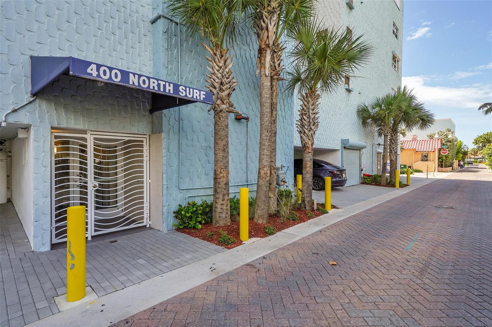 The exterior of a light blue building features a blue awning, palm trees, and bollards — 400 N Surf Road # 703, Hollywood FL 33019, HOLLYWOOD, FL