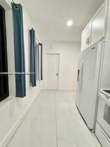 A narrow kitchen features white cabinets, a white refrigerator, and light-colored tile flooring — 2369 SW 17th Ter, Miami FL 33145, MIAMI, FL