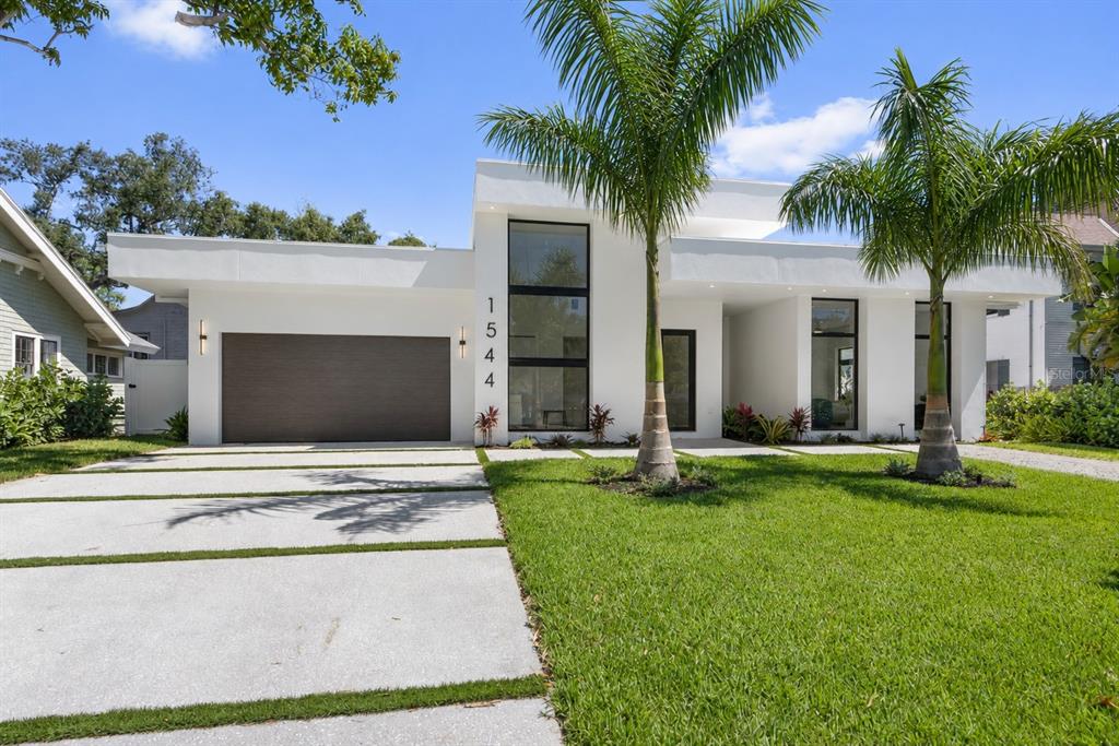 A modern white single-story house features a dark garage door, large windows, and palm trees — 1544 3RD AVENUE W, BRADENTON, FL