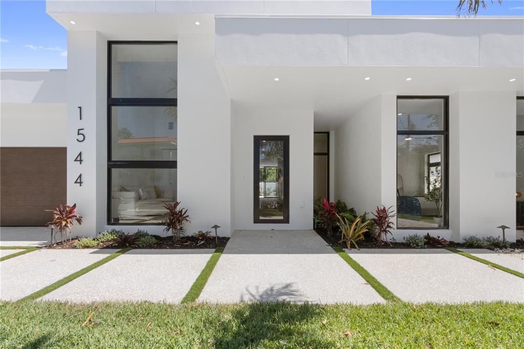 The exterior of a modern white house features large windows, a dark front door, and landscaping — 1544 3RD AVENUE W, BRADENTON, FL