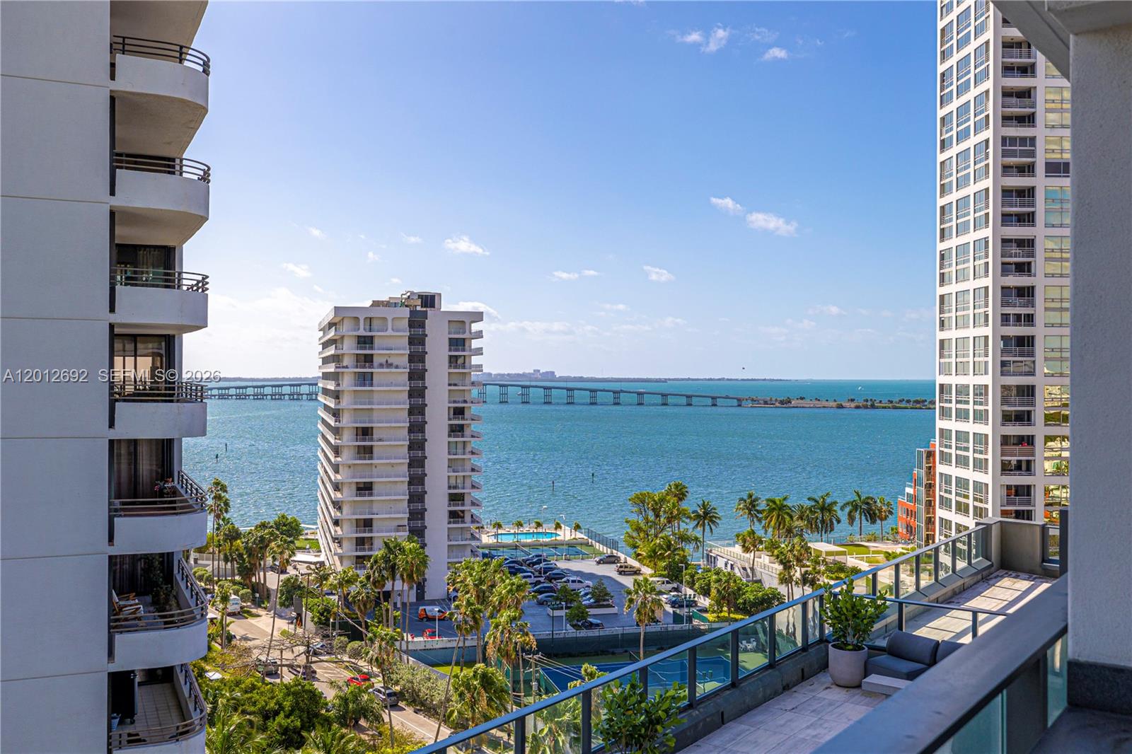 A balcony view overlooks a bay, a bridge, palm trees, and neighboring high-rise apartment buildings — 1451 Brickell Ave # 1002, Miami FL 33131, MIAMI, FL