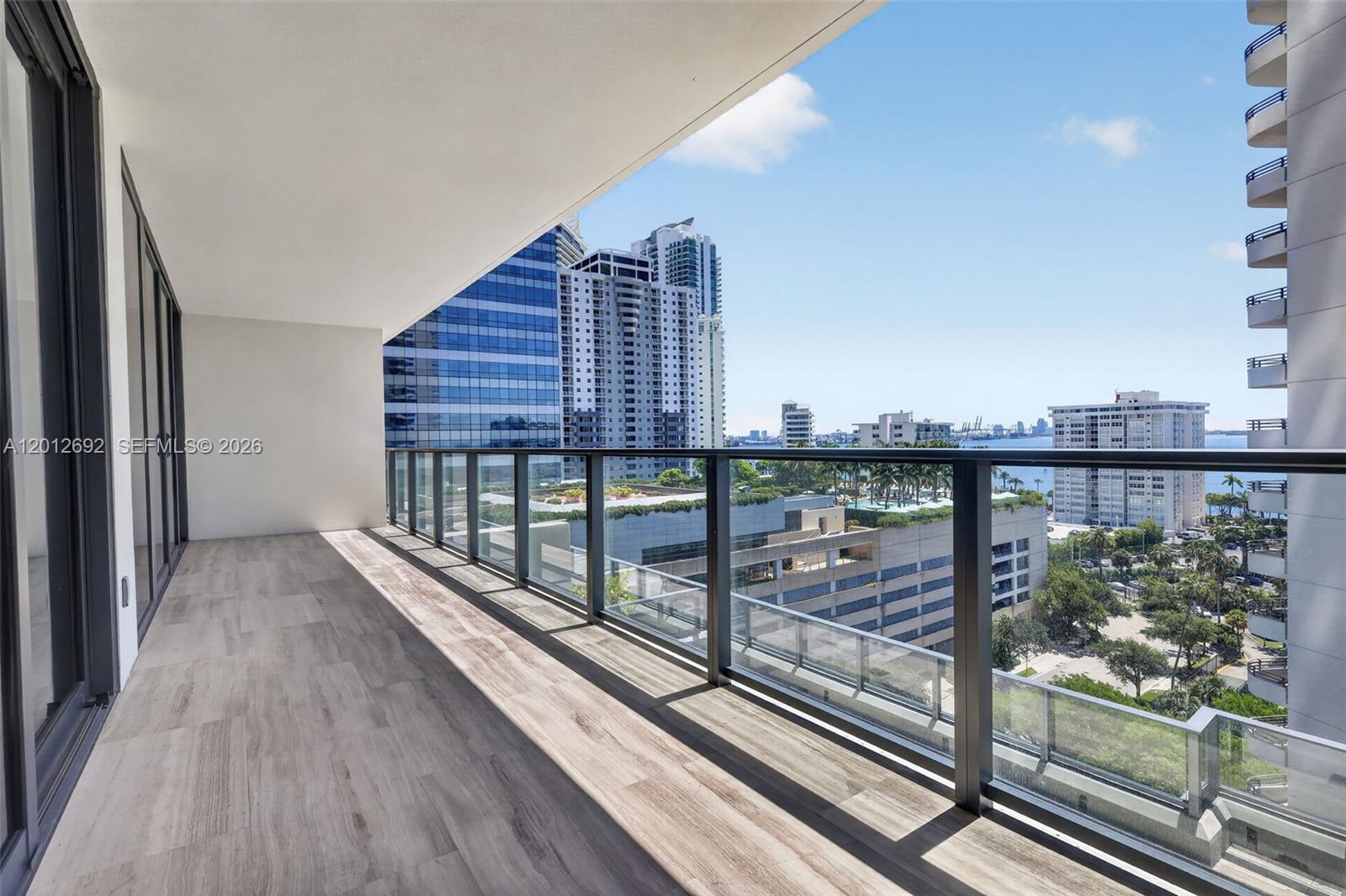 A modern balcony with wood-look tile flooring and a glass railing overlooks a city skyline — 1451 Brickell Ave # 1002, Miami FL 33131, MIAMI, FL