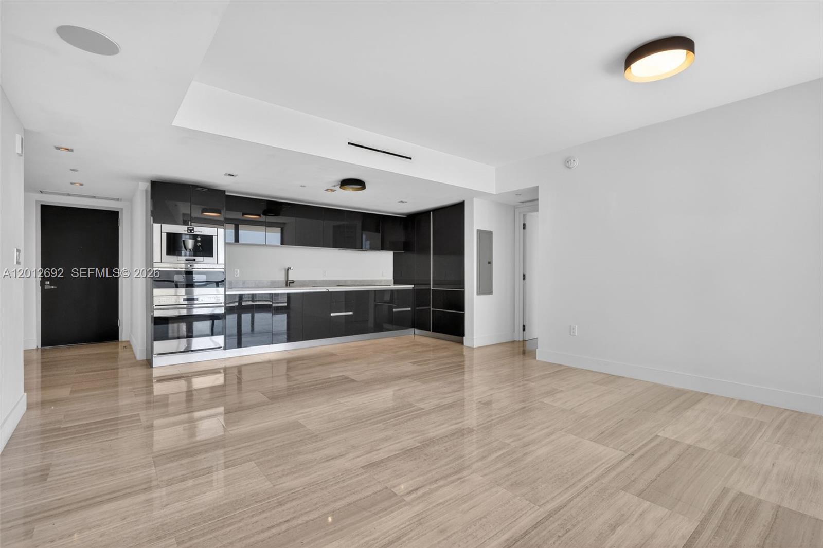 A modern kitchen with glossy black cabinets and light wood flooring in an open space — 1451 Brickell Ave # 1002, Miami FL 33131, MIAMI, FL