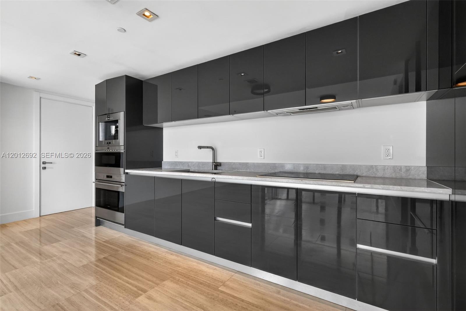A modern kitchen features glossy dark gray cabinets, stainless steel appliances, and light wood flooring — 1451 Brickell Ave # 1002, Miami FL 33131, MIAMI, FL