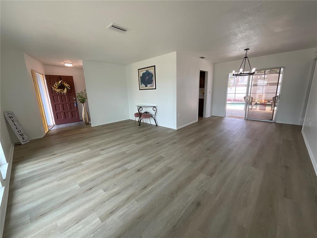 An open-concept living area features light wood-look flooring, a front entryway, and sliding glass doors — 2224 42ND STREET W, BRADENTON, FL