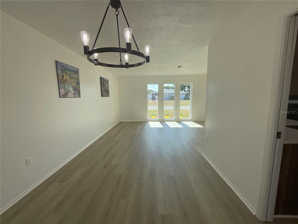 A dining area features light wood-look flooring, a black chandelier, and three large windows — 2224 42ND STREET W, BRADENTON, FL