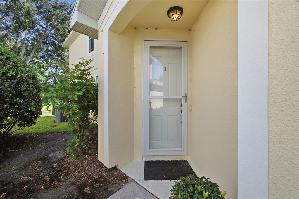 A light-colored front door with a storm door is set within a covered entryway — 485 HARBOR RIDGE DRIVE, PALM HARBOR, FL