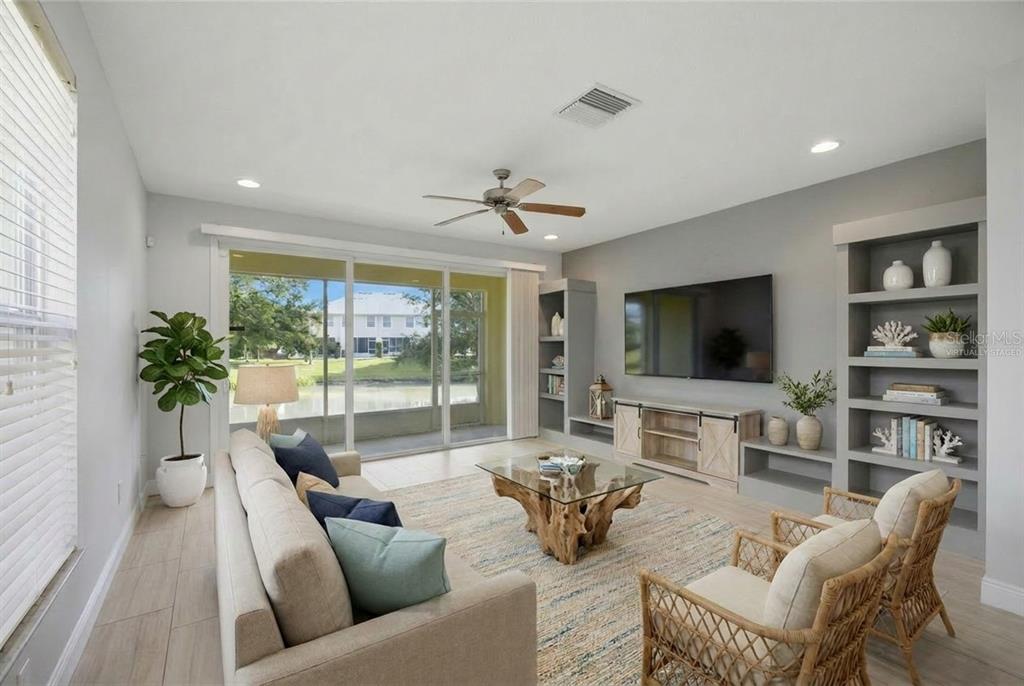 A living room with a large television, built-in shelving, a wood coffee table, and sliding doors — 485 HARBOR RIDGE DRIVE, PALM HARBOR, FL