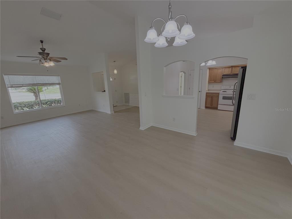 An open-concept living and dining area features light wood-look flooring and an arched kitchen opening — 10417 SW 52ND COURT, OCALA, FL