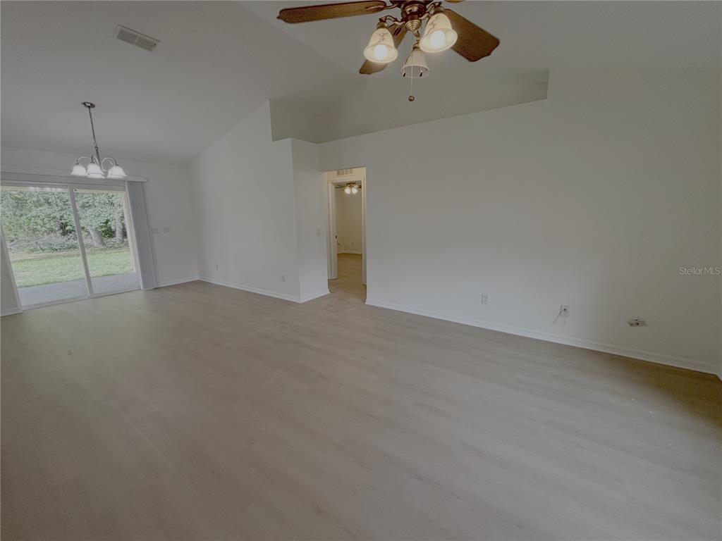 A spacious living room features light wood-look flooring, vaulted ceilings, and a sliding glass door — 10417 SW 52ND COURT, OCALA, FL