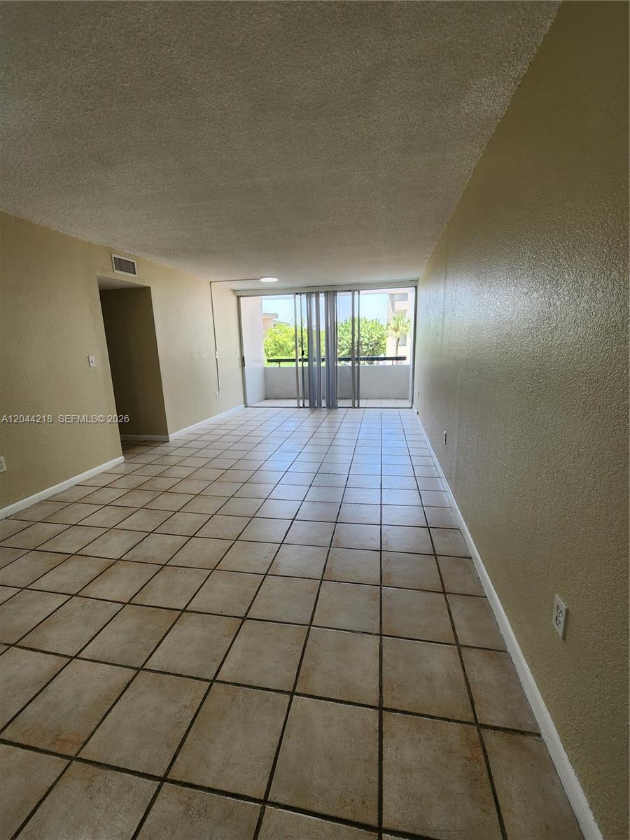 An empty room features beige tile flooring, light-colored walls, and a sliding glass balcony door — 802 NW 87th Ave # 312, Miami FL 33172, MIAMI, FL