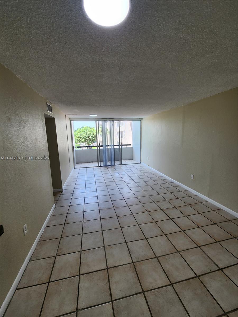 An empty living room features beige walls, tiled flooring, and a sliding glass door to a balcony — 802 NW 87th Ave # 312, Miami FL 33172, MIAMI, FL