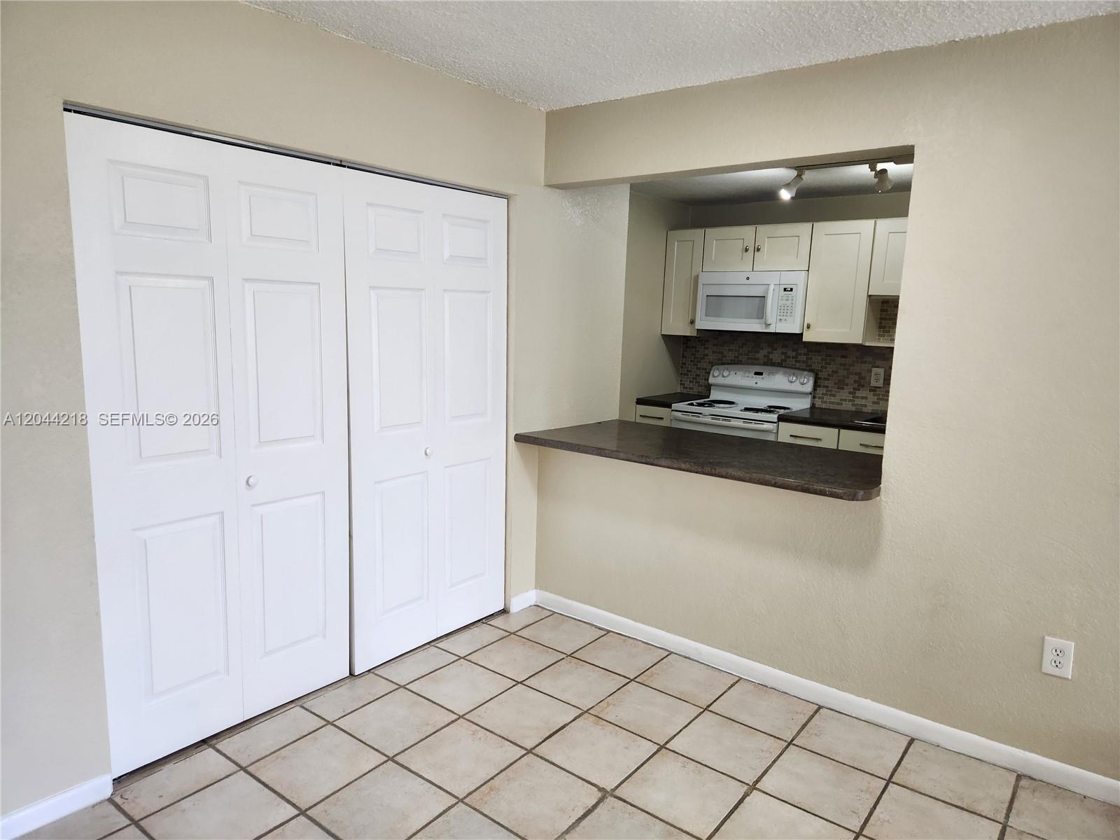 A kitchen with white cabinets and a breakfast bar opens into a tiled room — 802 NW 87th Ave # 312, Miami FL 33172, MIAMI, FL