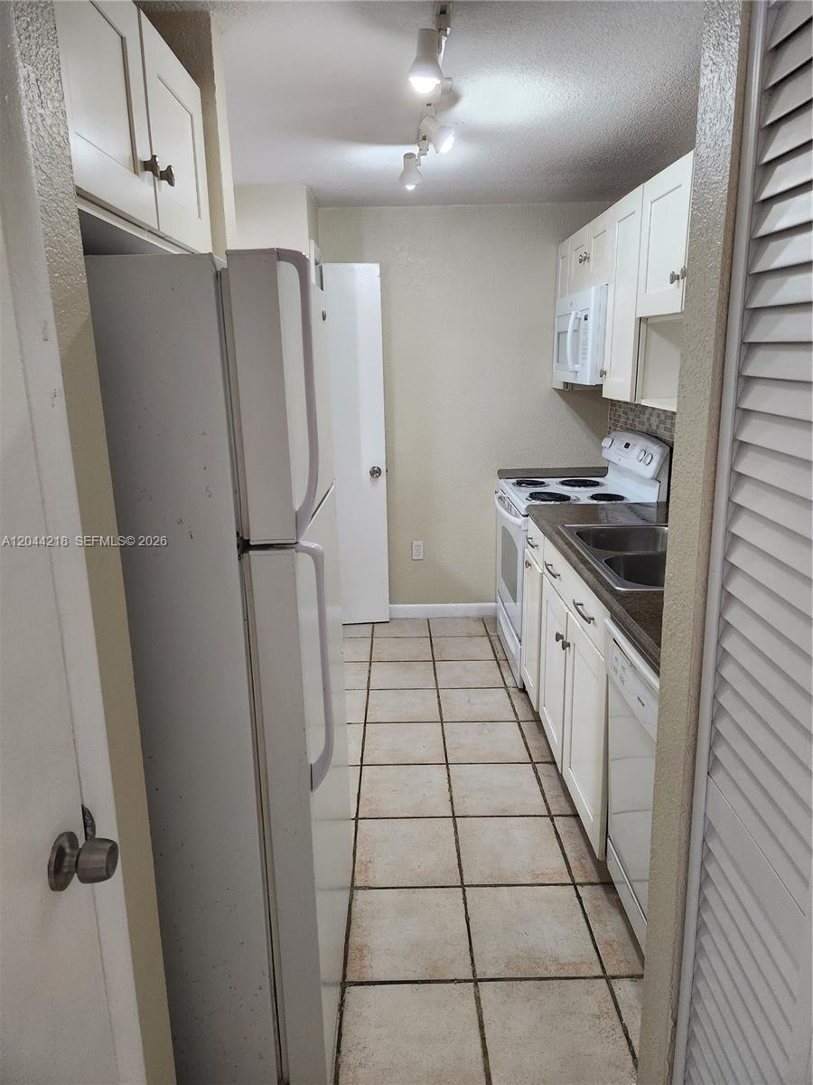A narrow galley kitchen features white cabinets, a white refrigerator, and light-colored floor tiles — 802 NW 87th Ave # 312, Miami FL 33172, MIAMI, FL