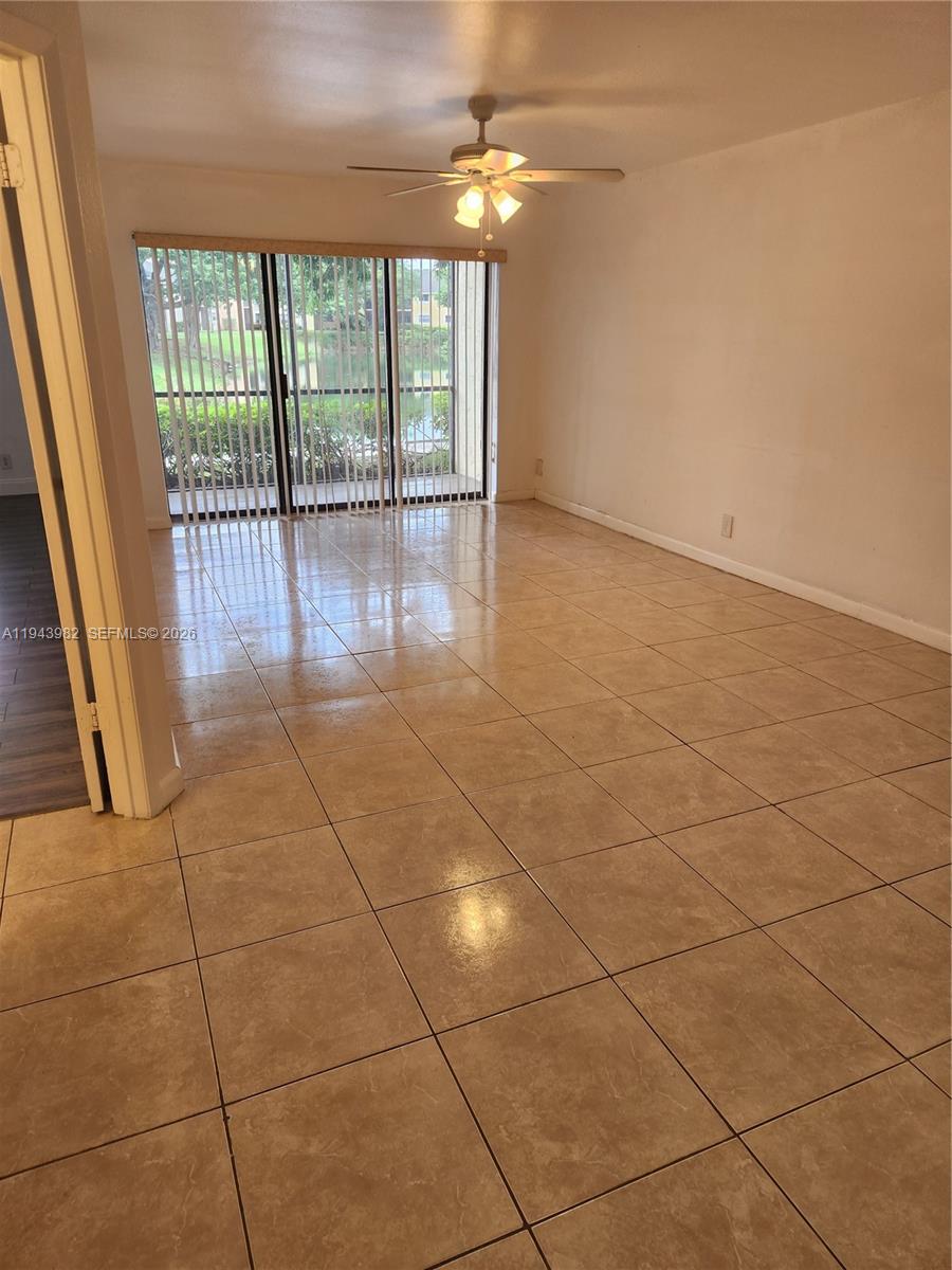 An empty living room features beige tile flooring, a ceiling fan, and sliding glass doors — 4086 N Pine Island Rd # 510, Sunrise FL 33351, SUNRISE, FL