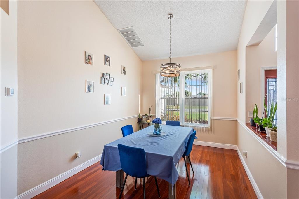 A dining room features a blue-clothed table, hardwood floors, a chandelier, and a window — 2821 LONE FEATHER DRIVE, ORLANDO, FL