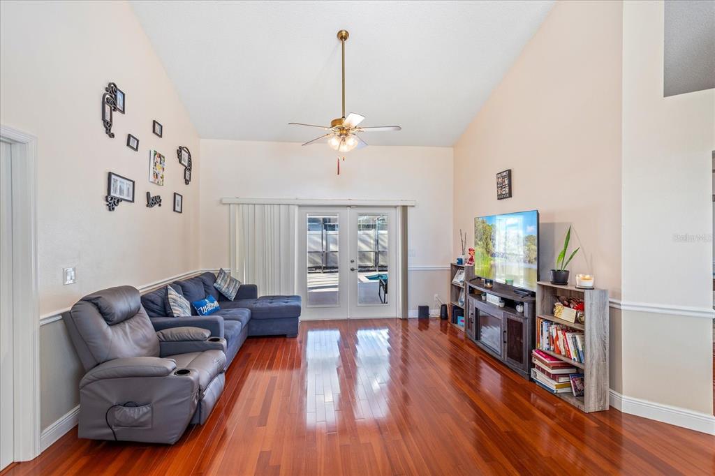 A living room features hardwood floors, a vaulted ceiling with a fan, and glass doors — 2821 LONE FEATHER DRIVE, ORLANDO, FL