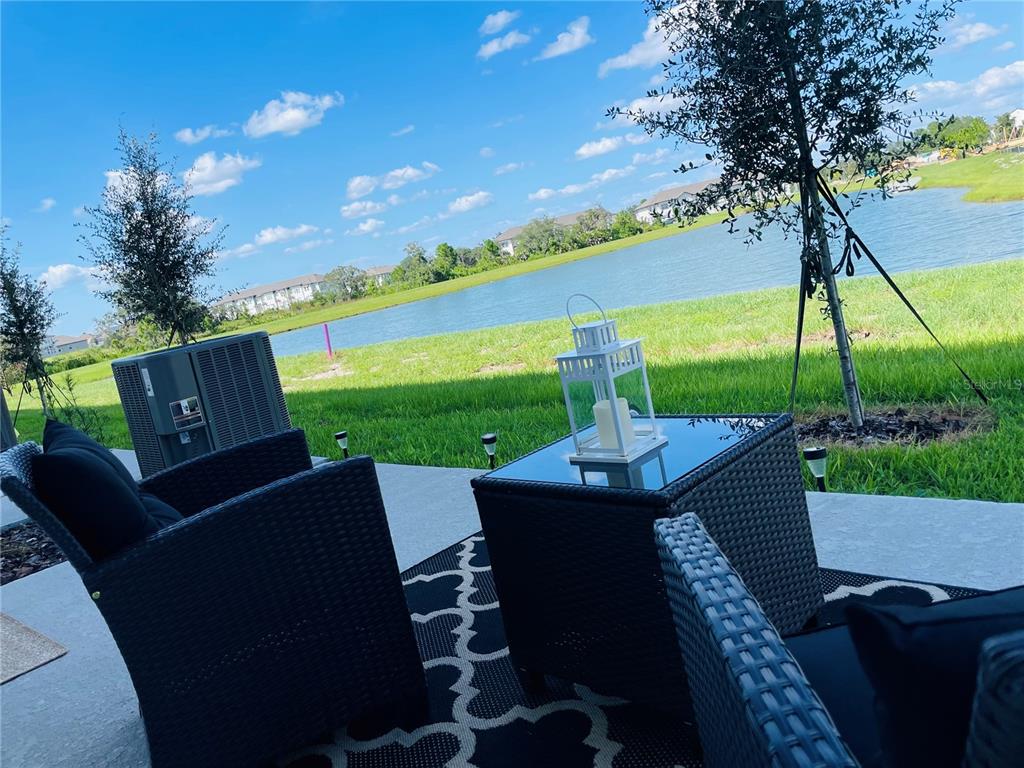 A patio with wicker furniture and a lantern overlooks a grassy lawn and a lake — 1039 PLANTATION LANE, DAVENPORT, FL