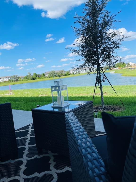 A patio with wicker furniture and a lantern overlooks a grassy lawn and a lake — 1039 PLANTATION LANE, DAVENPORT, FL